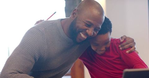 African american father and son learning together over laptop at home, sharing warm smile