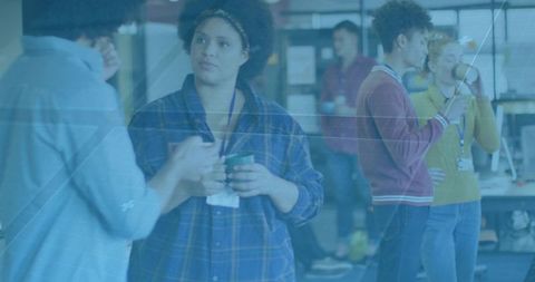 Mid-adult woman listening while holding coffee mug in open-plan coworking office with team