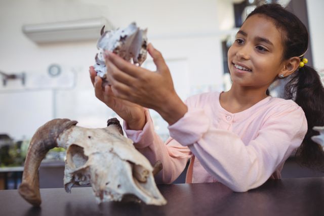 Happy elementary student examining animal skull by desk at science laboratory