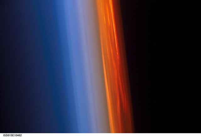 The image captures the stunning profile of the Earth's atmosphere illuminated by a setting sun, as seen from the International Space Station. The vibrant transition between dark space and the brightly colored atmosphere accentuates the beauty of orbited Earth. This striking depiction can be used for educational materials on astronomy, space exploration presentations, or in articles promoting the awe-inspiring revolutions made possible by space travel.