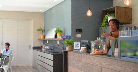 Barista serving fresh pastries at modern coffee counter with plants and daylight
