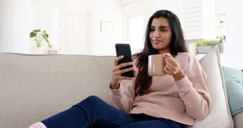 Relaxed Woman Sipping Coffee and Browsing Smartphone at Home