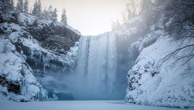 Winter waterfall plunging into frozen pool in snowy mountain gorge with icicles and mist