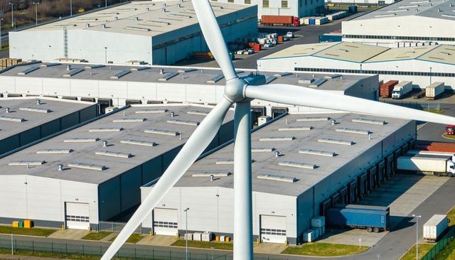 Wind turbine overlooking industrial logistics park with warehouses, loading docks, trailers