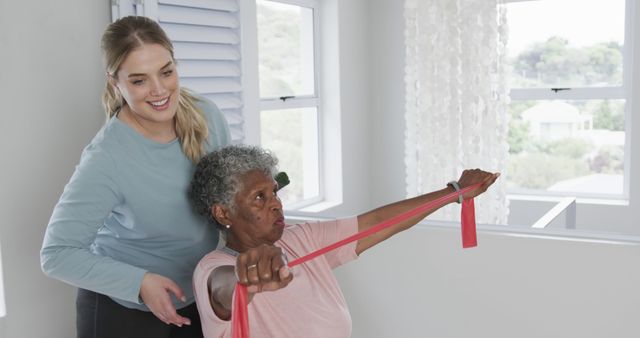 Senior woman engaging in exercise with the help of a personal trainer using a resistance band, illustrating themes of active aging, physical health, and rehabilitation. Ideal for use in advertisements for fitness programs, healthcare services targeting seniors, and wellness campaigns promoting healthy lifestyles for the elderly.