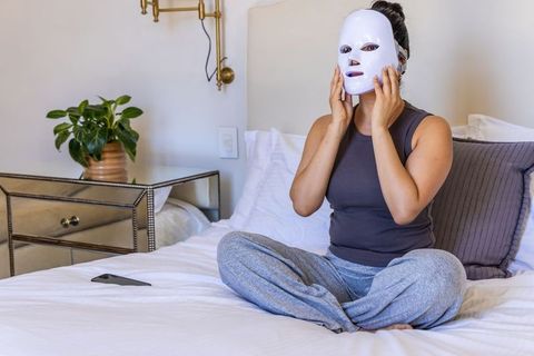 African american woman using led facial mask for at-home skincare and self-care on bed