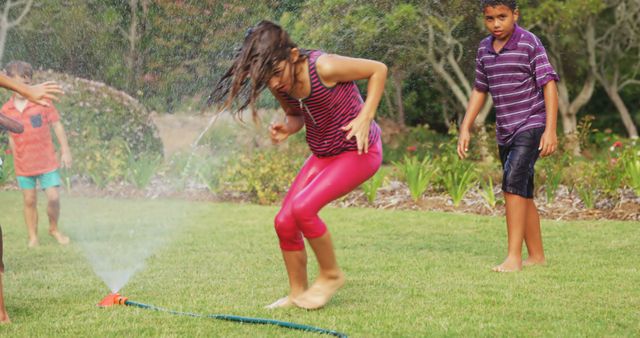 Group of children enjoying time outside playing with a sprinkler on a sunny day. Perfect for summer camp promotions, garden maintenance advertisements, childhood memories themes, and family outdoor activity articles.