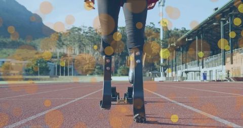 Male sprinter planting carbon fiber prosthetic blades in starting blocks on sunlit track