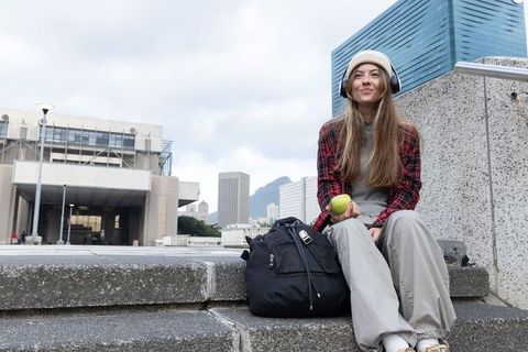 Young woman listening to music while holding green apple on city rooftop steps