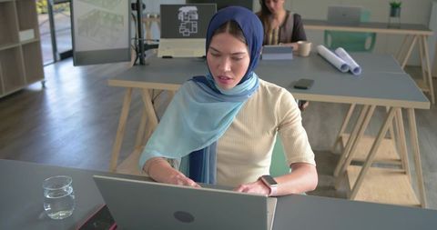 Indian woman collaborating in modern coworking office, using laptop and reviewing floorplan