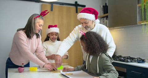Multigenerational family baking holiday cookies in modern kitchen wearing Santa hats