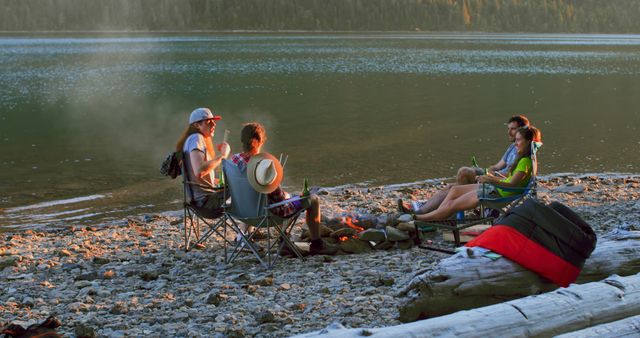 Friends sitting around campfire by calm lake during summer evening, enjoying nature and good company. Perfect for promoting outdoor activities, camping gear, adventure travel, or relaxation retreats.