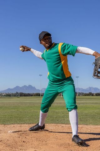 African american baseball pitcher delivering fastball on mound in green and yellow uniform