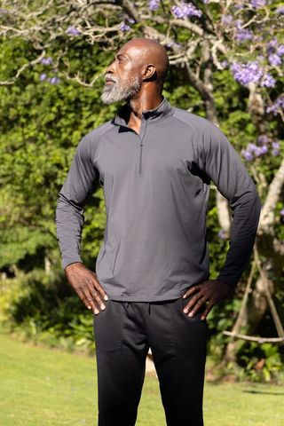 Confident mature man posing hands-on-hips in gray quarter-zip and black joggers in garden