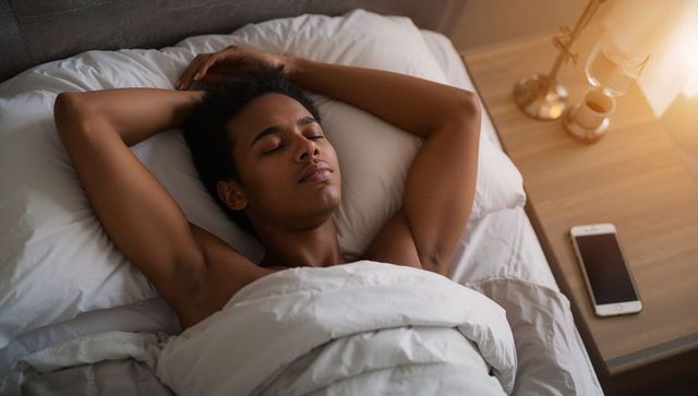 Sunlit morning resting bare-chested man sleeping under white duvet in cozy minimalist bedroom