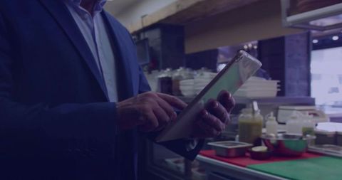Restaurant Manager Checking Tablet in Commercial Kitchen Prep Area Wearing Dark Blazer