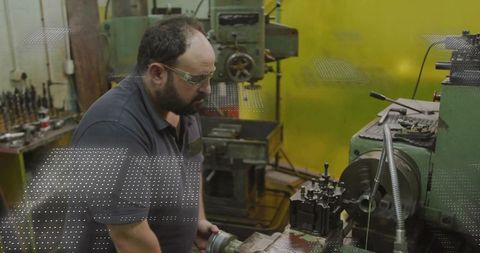 Machinist leaning over lathe in industrial workshop wearing safety glasses and polo shirt