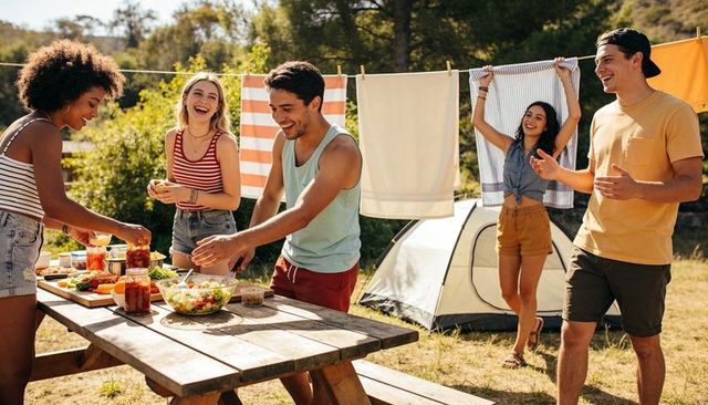 Friends camping picnic preparing summer meal at sunlit campsite with tent and clothesline
