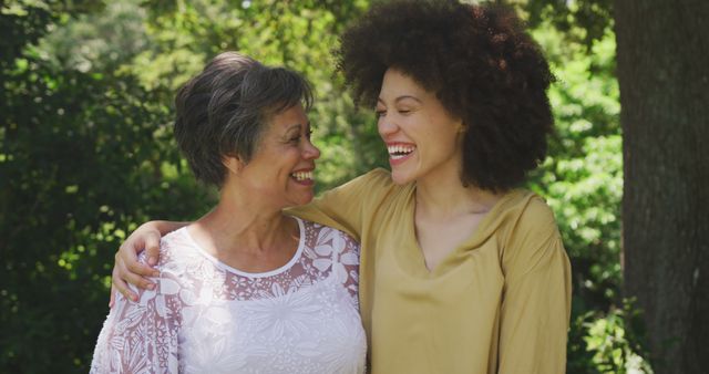 Happy biracial senior mother and adult daughter embracing and smiling at each other in garden. Family, motherhood, nature and togetherness.