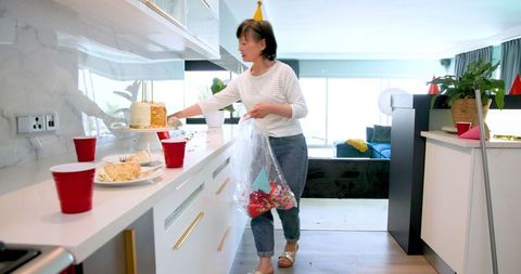 Senior Woman Tidying Up After Festive Birthday Celebration in Kitchen