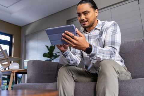 Young man sitting on sofa using tablet for remote work in modern living room