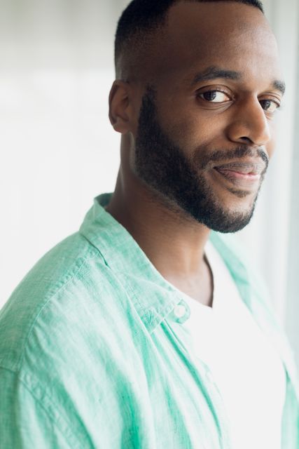 This image shows an African-American man smiling while standing inside a white room. He is wearing a green shirt and has a beard. The photo can be used for promoting positivity, confidence, and casual lifestyle themes. It is suitable for use in advertisements, blogs, and social media posts focusing on personal development, fashion, or everyday life.