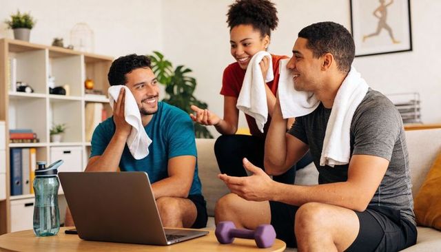 Friends cooling down after home workout with laptop, dumbbell and water bottle