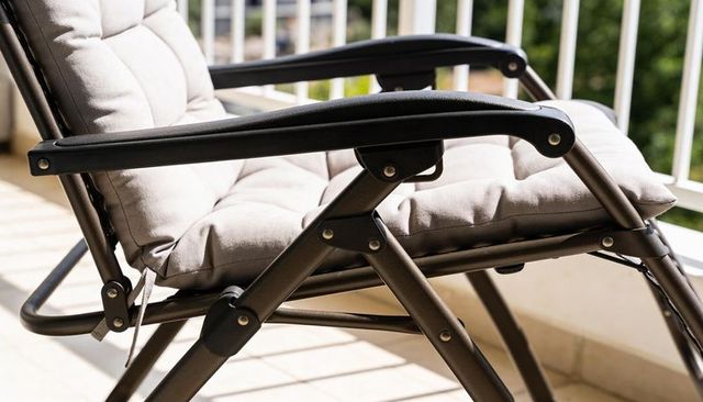 Tufted beige folding lounge chair on sunlit balcony with padded cushion and metal frame