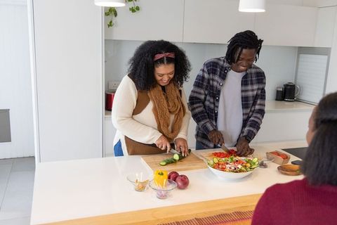African american couple chopping vegetables and preparing salad at modern kitchen island