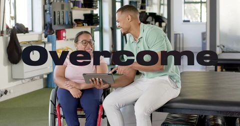 Overcome: smiling wheelchair patient and therapist using tablet in rehab clinic