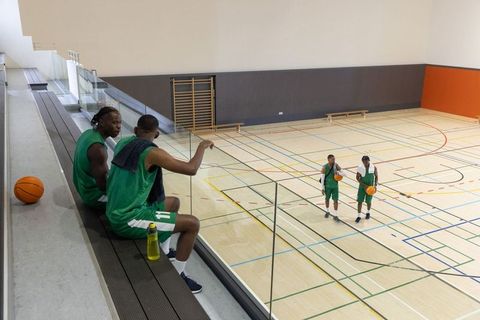 Basketball teammates resting on bleachers overlooking indoor court during practice and drills