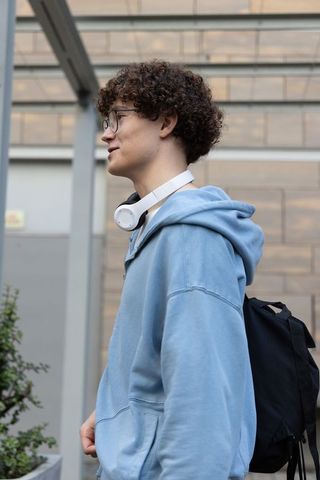 Teen male wearing headphones and backpack standing in urban entrance profile portrait
