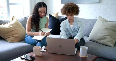 African American Women Collaborating on Laptop and Notebook in Cozy Home Living Room