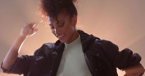 Backlit african-american woman dancing in leather jacket and ribbed top, hoop earrings