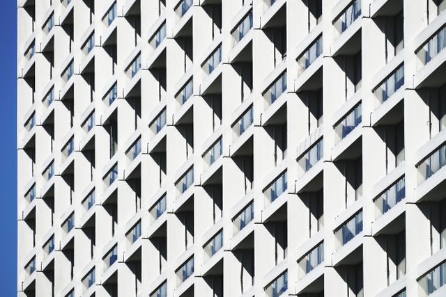 Image showcasing repetitive geometric patterns on a modern building facade, with numerous windows placed in a symmetrical arrangement. Ideal for use in architectural blogs, urban design portfolios, articles on modern construction techniques, and presentations related to contemporary architecture.
