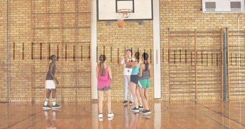 Coaching teen basketball team during shooting drill in school gymnasium