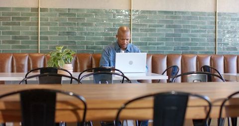 African american man working on laptop in minimalist cafe banquette with green tiles