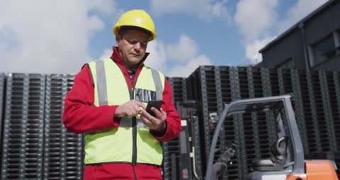Warehouse Worker Using Phone Outdoors Near Stacked Crates