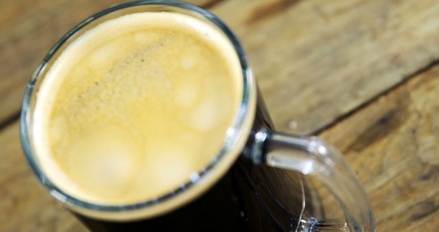 A close-up view of a freshly brewed cup of coffee with a frothy top, placed on a wooden surface. Its inviting appearance suggests a moment of relaxation or a quick energy boost during a busy day.