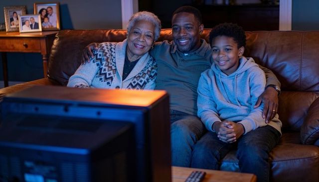Multigenerational family relaxing on couch watching tv with remote in cozy living room