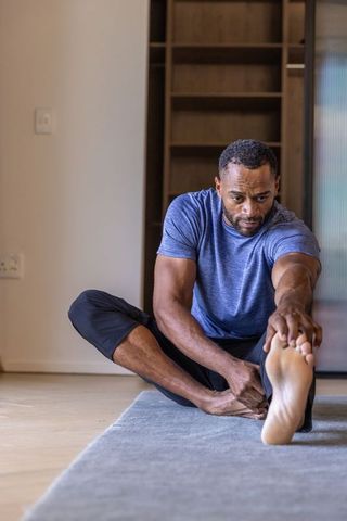 African american man stretching hamstring at home on mat reaching for toe fitness routine