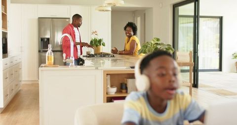 African american family cooking in bright modern kitchen, child using headphones