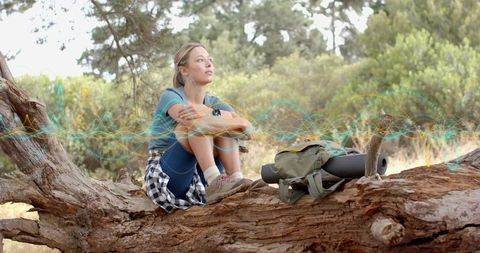 Thoughtful hiker sitting on fallen log hugging knees with backpack and waveform overlay