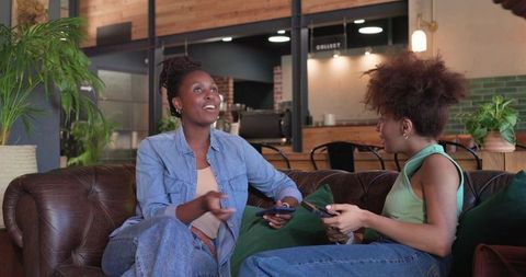 African American Friends Chatting on Leather Sofa in Cozy Urban Cafe with Smartphones