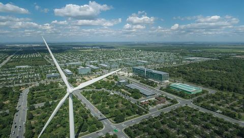 Wind turbine towering over green corporate campus and suburban sustainable landscape