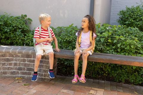 Children chatting on bench with backpacks in sunny courtyard