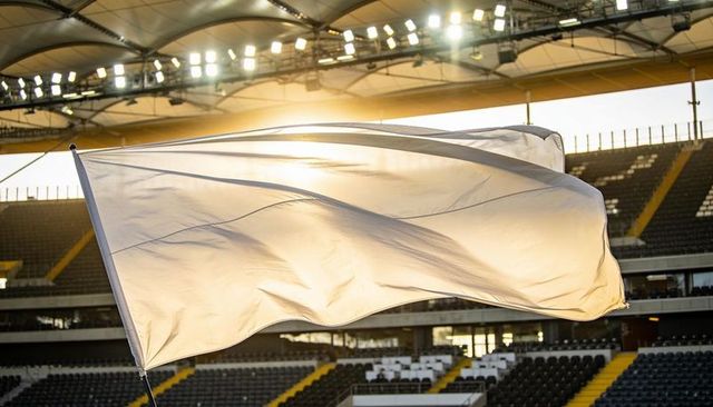White flag billowing in sunlit stadium at golden hour, empty stands and arena lights