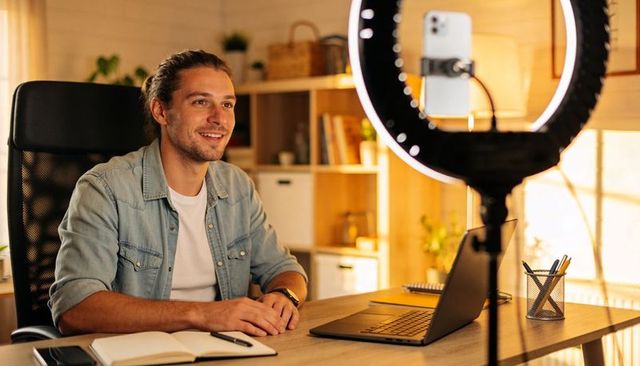 Content creator recording with ring light in cozy home office with laptop and smartphone