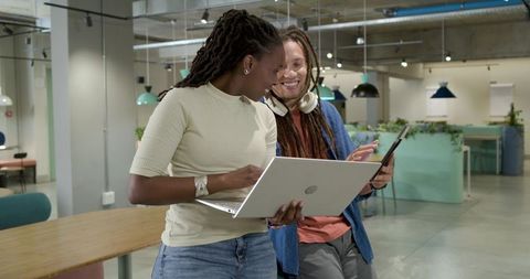 Young Professionals Collaborating with Laptop and Tablet in Modern Coworking Workspace