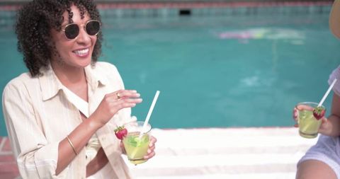 Diverse friends sipping green cocktails poolside, relaxing sunglasses, strawberry garnish